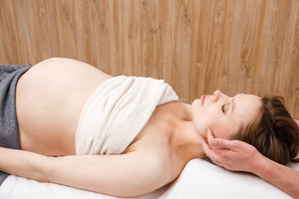 Pregnant woman receiving osteopathic treatment in a clinic. Manual therapist manipulates woman's head